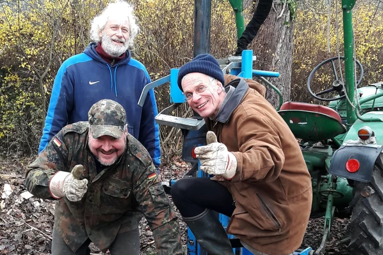 Drei Männer stehen vor einem landwirtschafltichen Fahrzeug. Sie tragen winterliche Kleidung und Handschuhe und halten lächelnd den Daumen nach oben in die Kamera