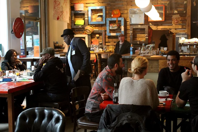 Einblick in eine Kneipe oder ein Café. Menschen sitzen an Tischen trinken Kaffee und unterhalten sich.