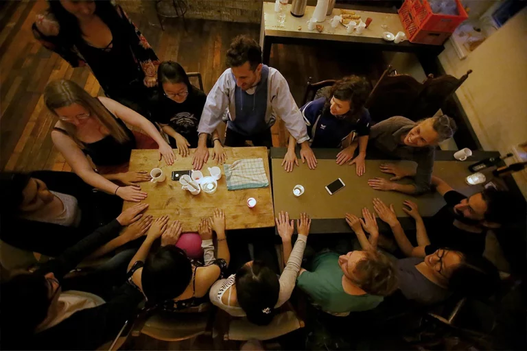 Gruppe von Menschen von oben aufgenommen, an einem Tisch sitzend. Sie halten ihre Hände auf den Tisch für ein Spiel.